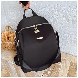 Detail of black nylon backpack featuring gold metal zippers and brand logo plate