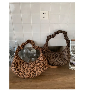 Detail of two hobo bags featuring leopard print and ruched handles on a wooden table