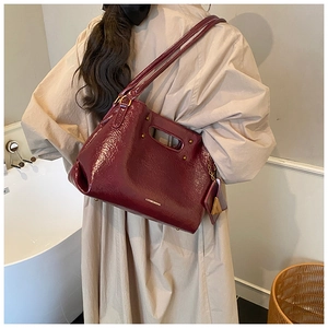 Detail of burgundy patent leather handbag on trench coat showing sleek handle and texture