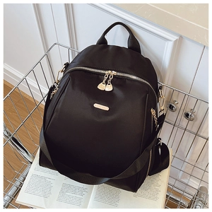 Detailed view of black nylon backpack featuring gold metal logo and dual zipper closure