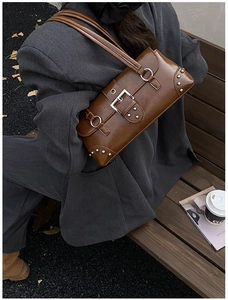 Détail du sac sous l'aisselle en cuir marron foncé avec clous argentés et boucle en métal