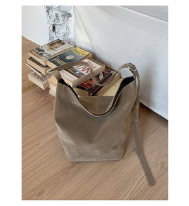 Detail of a brown suede tote bag with metallic eyelet strap on a light wood floor