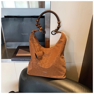 Détail du sac hobo léopard avec poignée en perles de bois et logo métallique sur une chaise