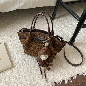 Detail of leopard print bucket bag with brown leather handle and cute plush bear charm