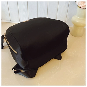 Close-up of black oxford fabric backpack with gold zippers and metal logo plate detail