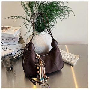 Détail du sac demi-lune en daim marron foncé avec pompon bohème et fine bandoulière
