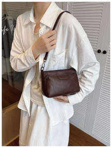 Detail of a dark brown textured leather crossbody bag with a front zip pocket on a model