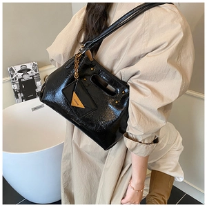 Detail view of black patent leather tote bag with gold rivets on beige trench coat