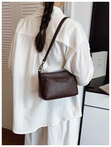 Detail of dark brown pebble leather crossbody bag showing zipper pocket and metal hook