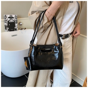 Detail view of a black glossy shoulder bag with pleated texture and metal chain charm