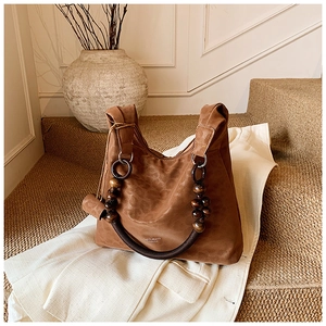 Détail du sac hobo en daim avec poignée en perles de bois et logo dans un décor de studio