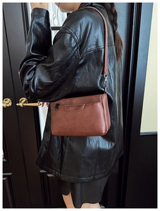 Brown vintage style leather crossbody bag shown on a model wearing a black jacket