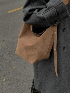 Vintage brown suede tote bag with metal eyelets worn by model in a street style shot