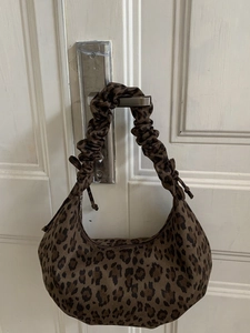 Leopard print crescent hobo bag with scrunchie shoulder strap hanging on a door handle
