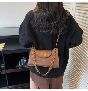Détail d'un sac bandoulière vintage marron avec chaîne dorée et fermoir pivotant en métal