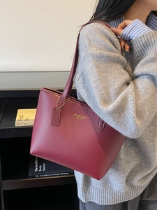 Grand cabas rouge bordeaux en cuir grainé avec logo doré porté par un mannequin