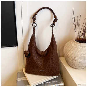 Détail du sac hobo léopard avec poignée en perles de bois sur une valise grise