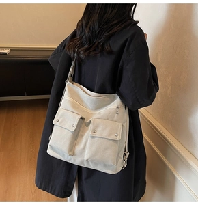 Rear view of a light gray canvas crossbody tote bag worn over a black winter coat