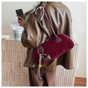 Detail of burgundy suede baguette bag worn on shoulder featuring decorative mini leather pouch