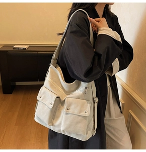 Detail der cremeweißen Canvas-Hobo-Tasche mit zwei Vordertaschen und Metalldruckknöpfen