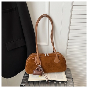 Detail of vintage brown suede bowling bag with mini charm on a textured suitcase