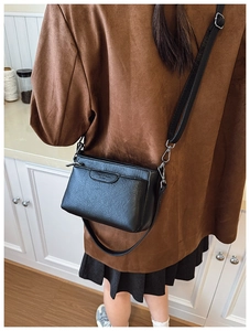 Detailed view of the black textured crossbody bag worn by a model in a cozy home setting