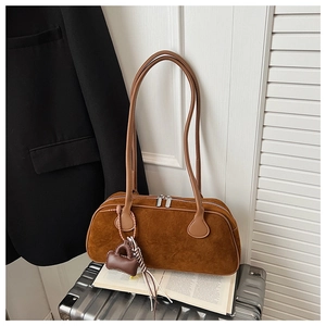Detail of caramel matte leather bowling bag with long handles and decorative charm on luggage