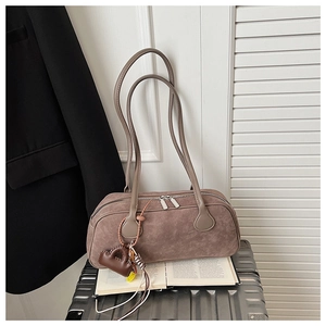 Close-up of taupe suede pillow bag with dual zippers placed on an open book in a modern room