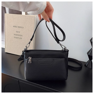 Detail of black PU leather crossbody bag featuring front zipper and embossed logo texture