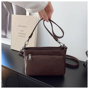 Detail view of brown minimalist crossbody bag with front zipper pocket on a sideboard