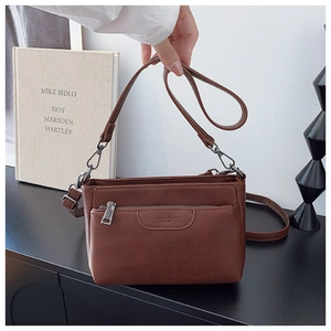 Detail view of the brown leather crossbody bag showing the front zipper and logo texture