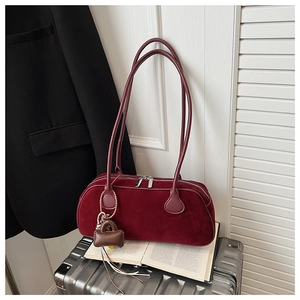 Detail of burgundy suede shoulder bag with dual zippers and decorative mini charm