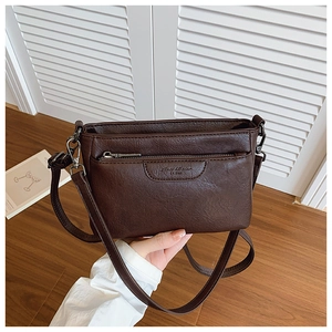 Detail of dark brown leather crossbody bag featuring front zipper pocket and embossed logo