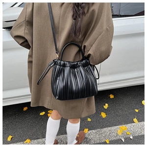 Detail of a black pleated bucket bag with a top handle and slim shoulder strap