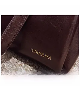 Macro shot of dark reddish brown leather texture and gold brand logo on the handbag