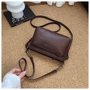 Close-up of litchi texture brown crossbody bag with zipper pocket and metal strap hook