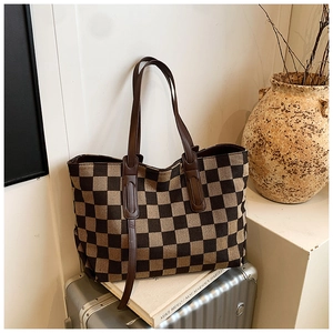 Chic checkered tote bag with brown straps displayed on a travel suitcase with dry branches