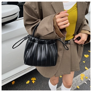 Detail of black pleated bucket bag with drawstring and thin handles on a street background
