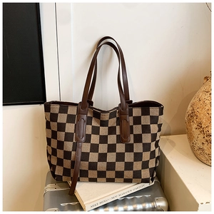 Detail of checkered tote bag with brown leather straps displayed on a silver suitcase
