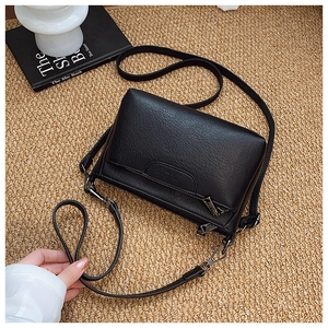Detail of black pebbled leather crossbody bag with flap zipper and elegant metal hardware