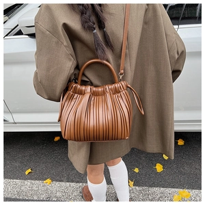 Detailed view of brown pleated crossbody bucket bag with round handles in a street setting
