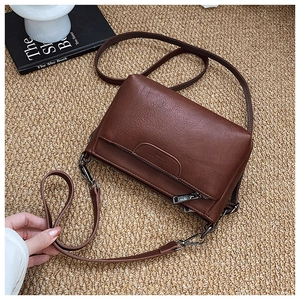 Close-up of brown pebbled leather crossbody bag featuring multi-layer zipper compartments