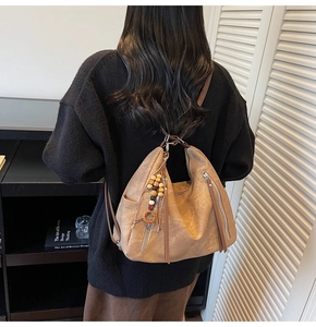 Detail of camel brown tote bag featuring wooden beads tassel and metallic side zippers