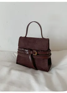Detalle de bolso de ante marrón oscuro con correas de cuero vintage y hebillas metálicas