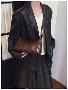 Detail of dark brown glossy leather crossbody bag with gold text on black blazer