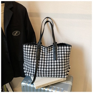 Close-up of houndstooth tote bag texture and leather handle on a silver suitcase