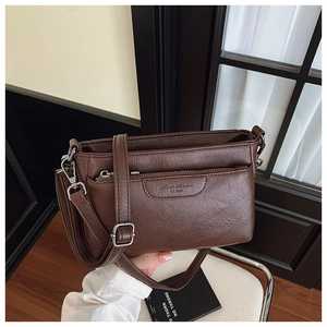 Detail of dark brown leather crossbody bag with front zipper pocket and embossed logo