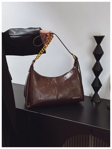 Close-up of glossy dark brown patent leather bag with gold chain strap detail