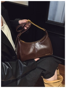 Detail of glossy brown hobo bag featuring gold chain handle and brand lettering