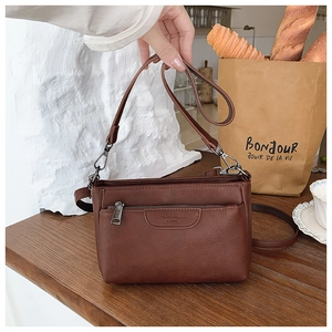 Detailed close-up of brown leather crossbody bag with front zipper pocket on wooden table